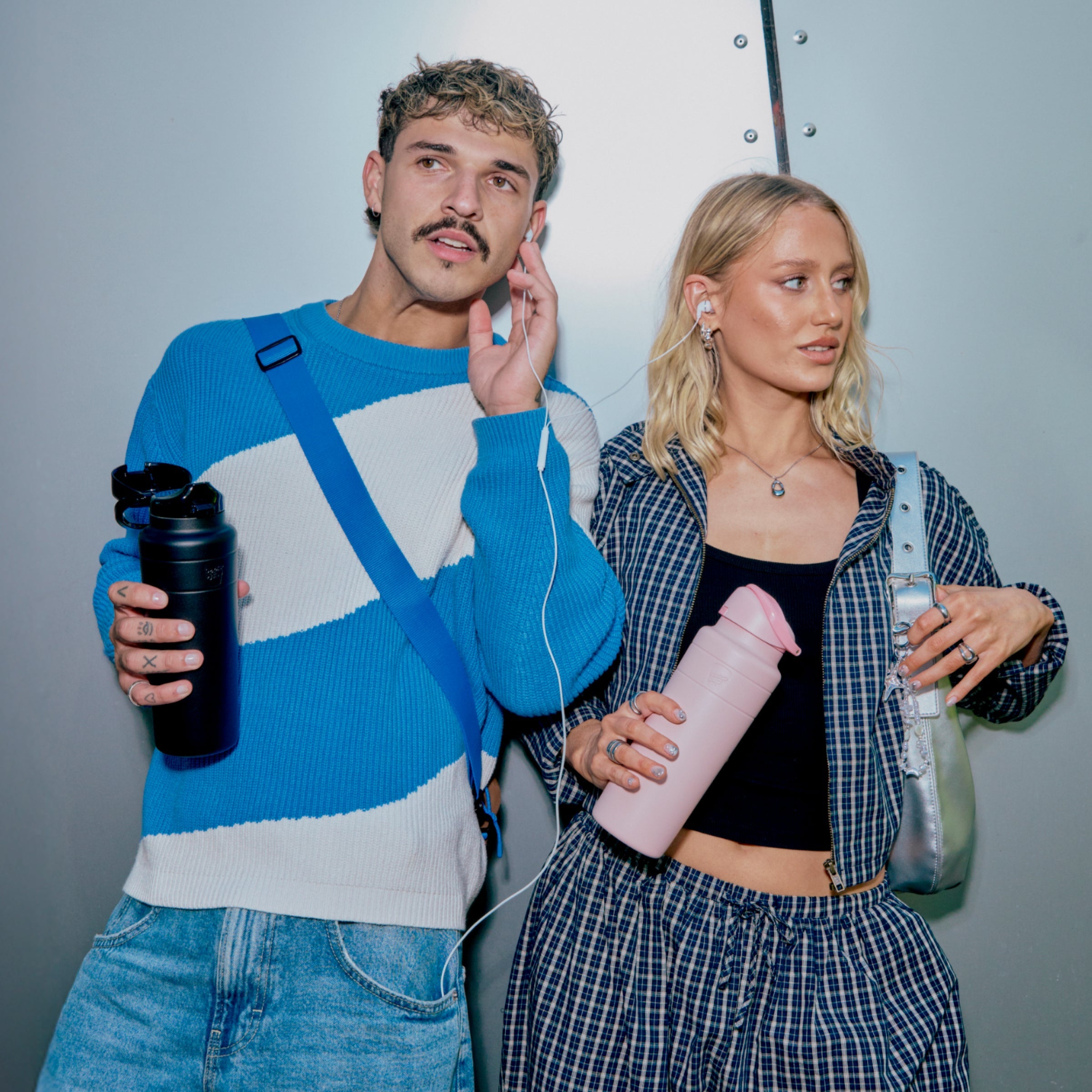 Two people standing side by side, each holding a water bottle, against a plain background.