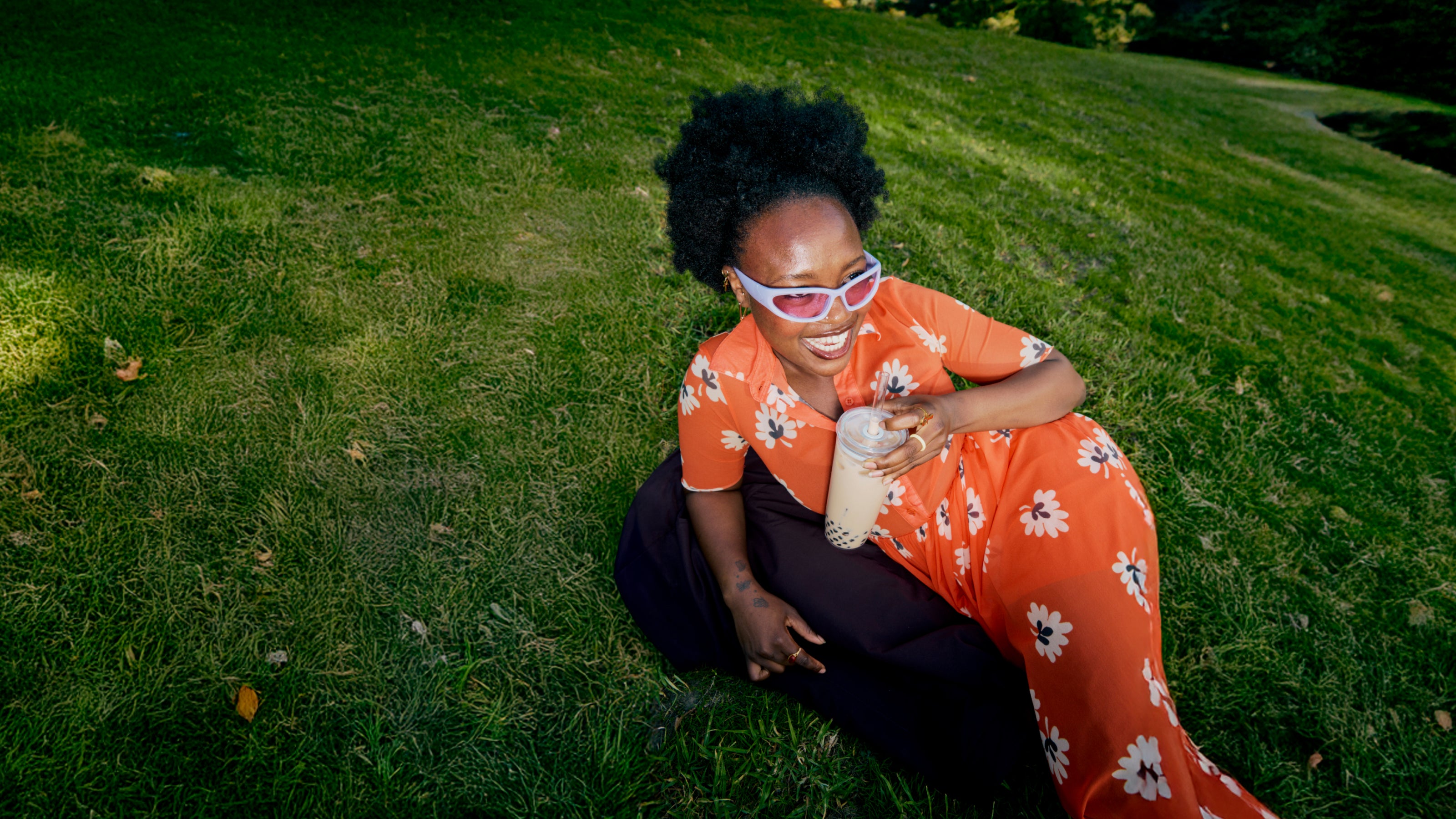 Person wearing an orange floral dress sitting on grass