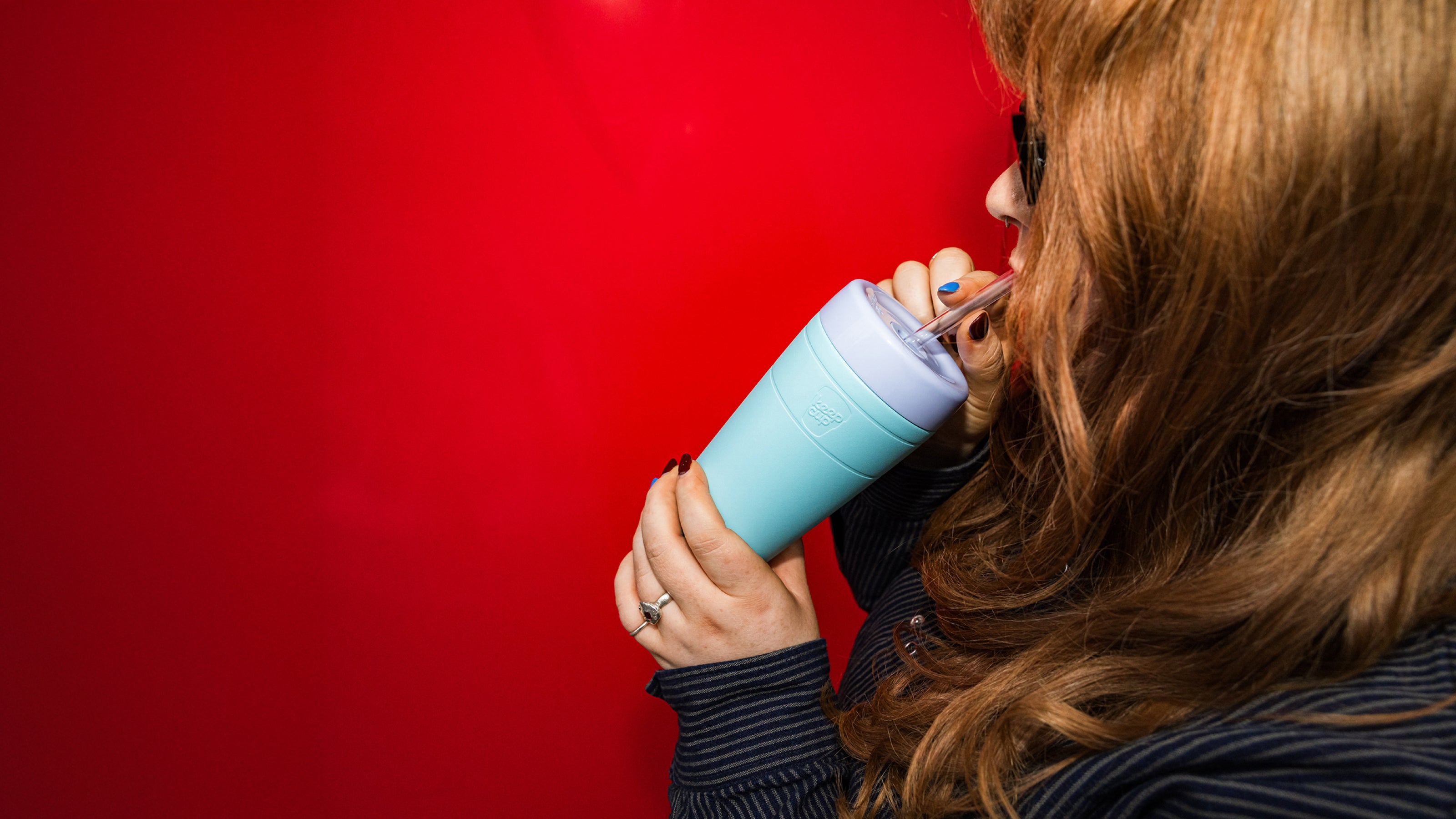 Person holding a turquoise tumbler against a red background