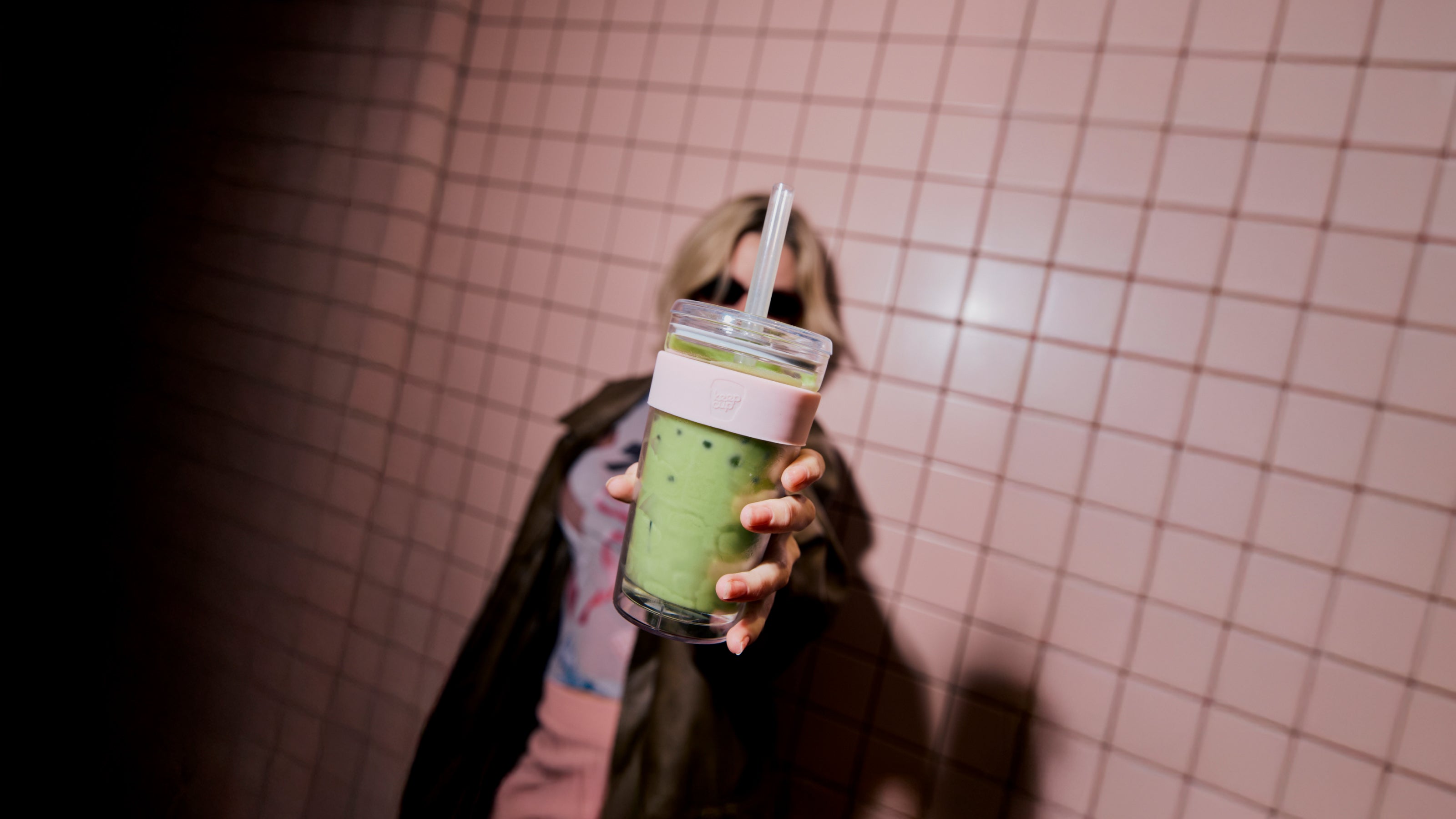 Person holding a green smoothie in a tumbler with a checkered wall background