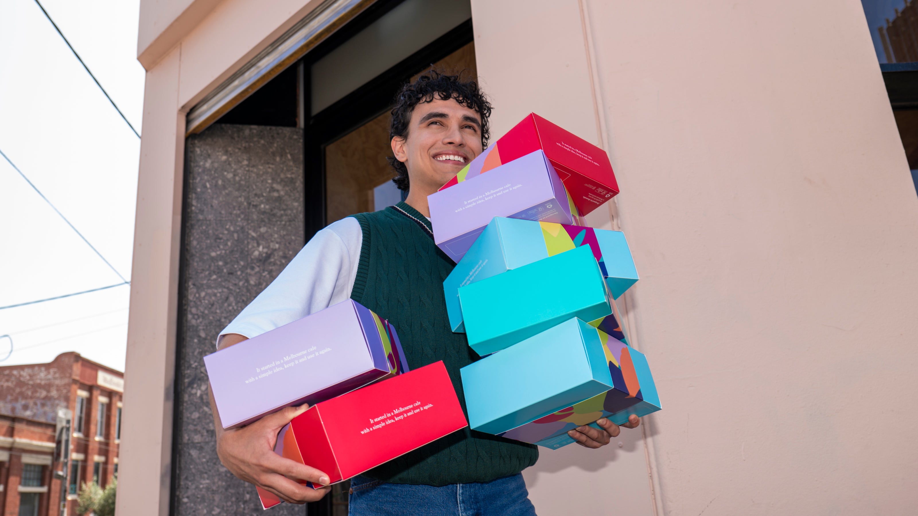 Person holding a stack of colorful boxes outside a building