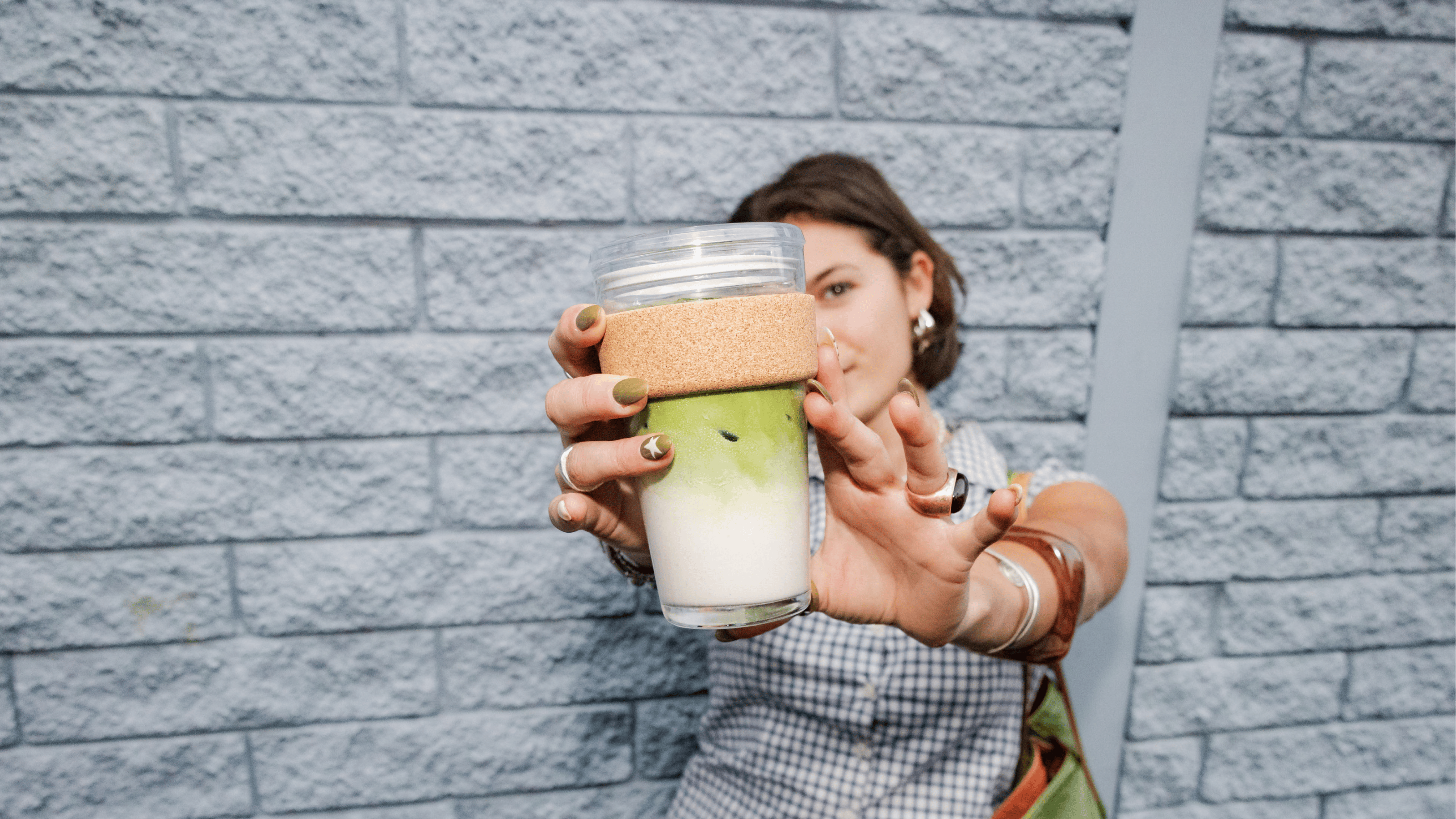 Person holding a reusable coffee cup against a gray brick wall