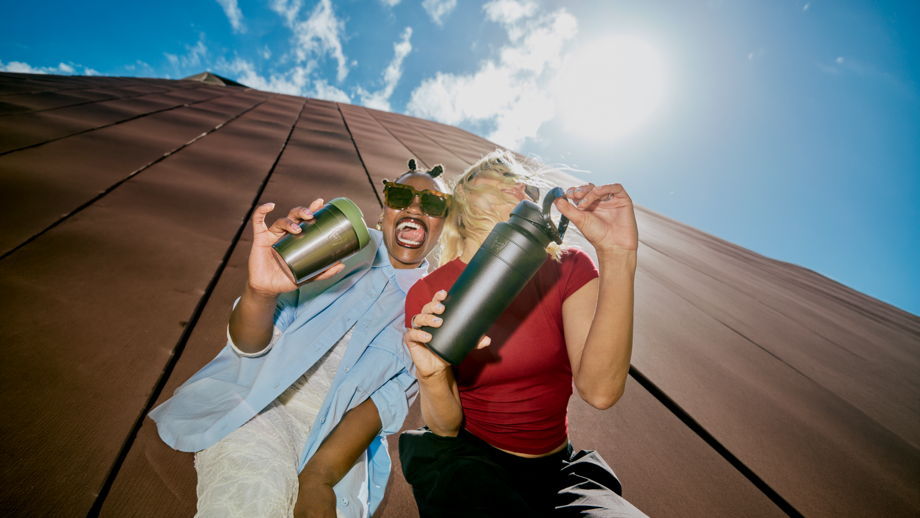 Two girls under a blue sky holding a Commuter in Nitro Pine and Ora Bottle