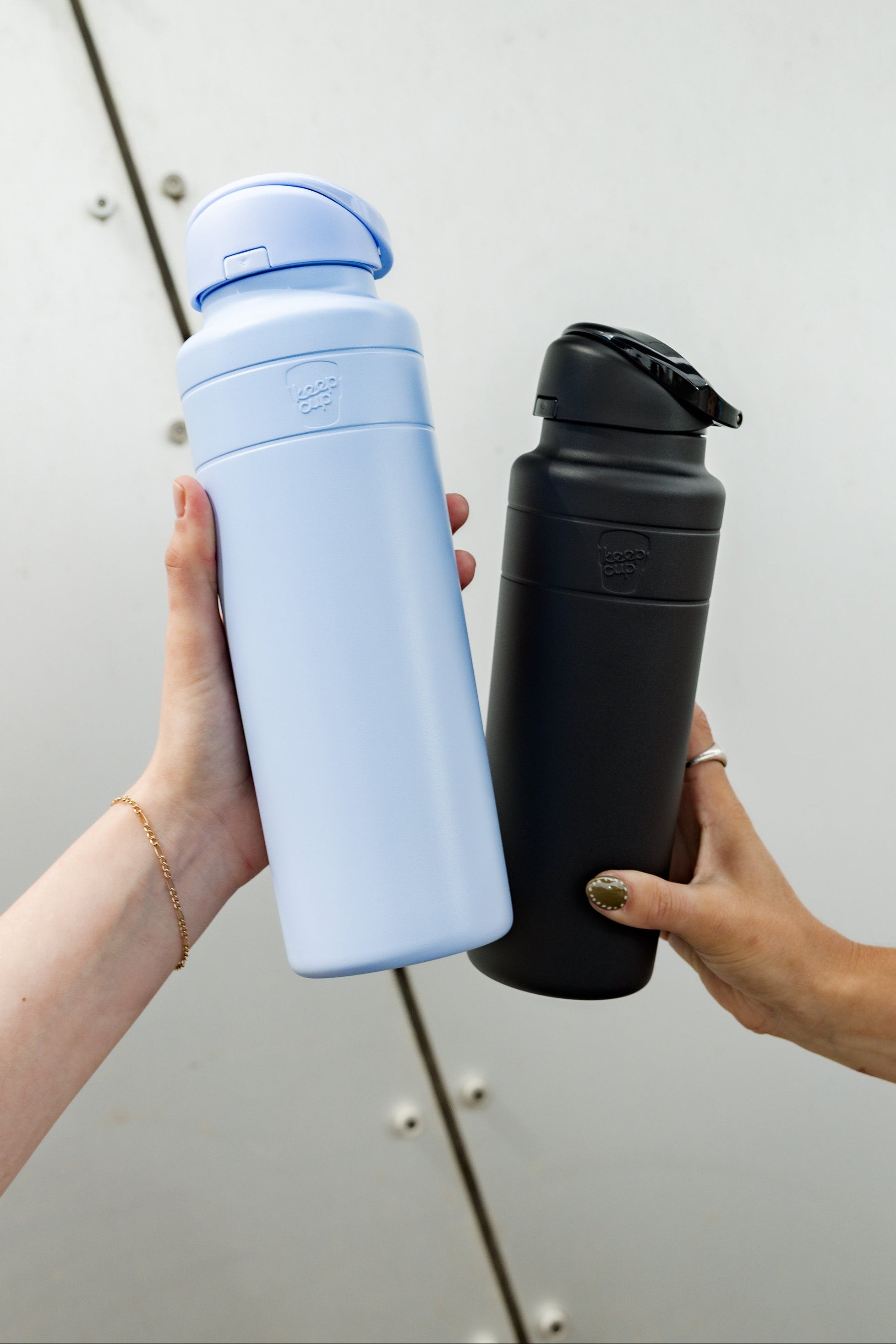 Two hands holding a orchid and a black water bottle against a neutral background
