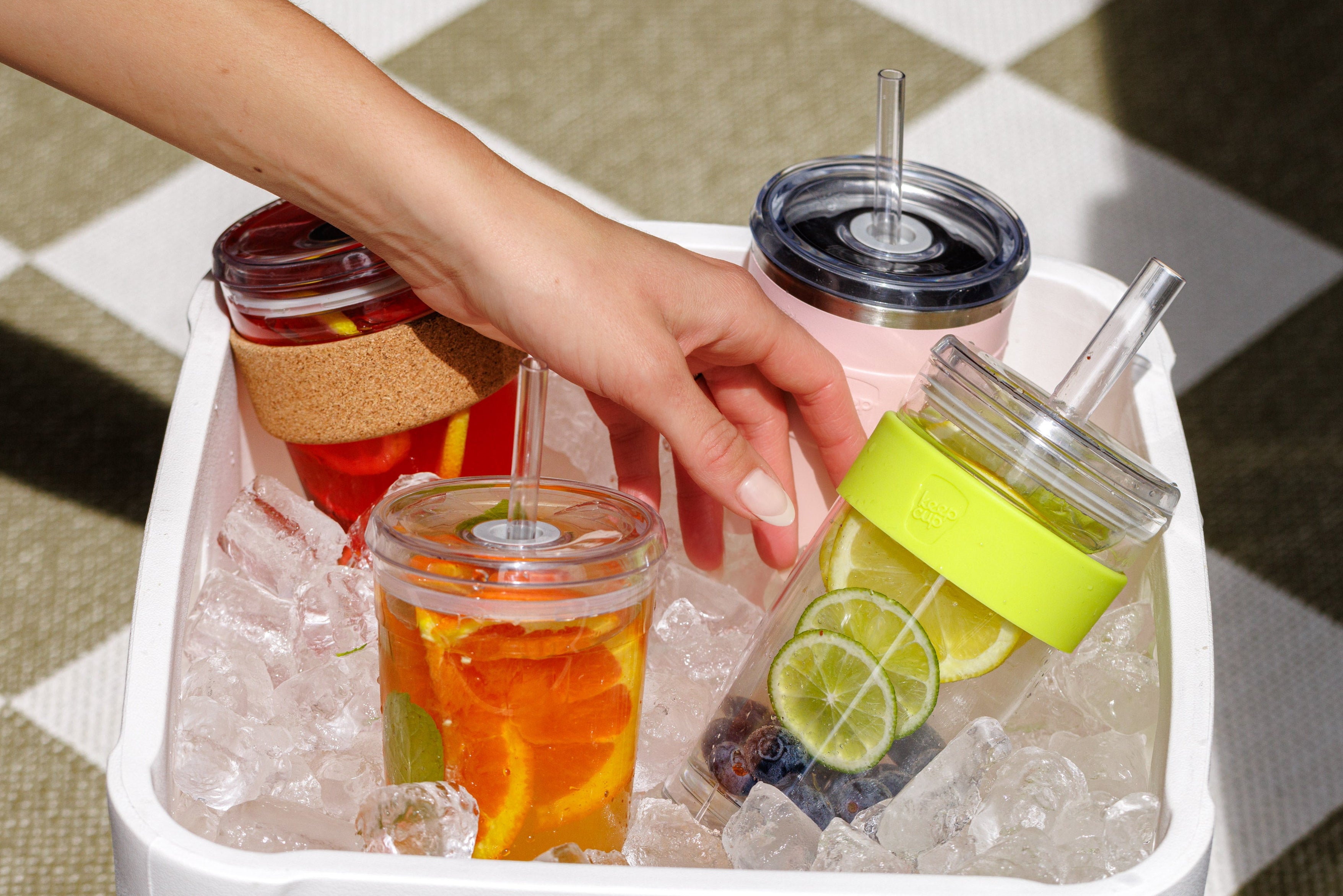Hand reaching for a drink in a insulated container filled with ice and drinks.