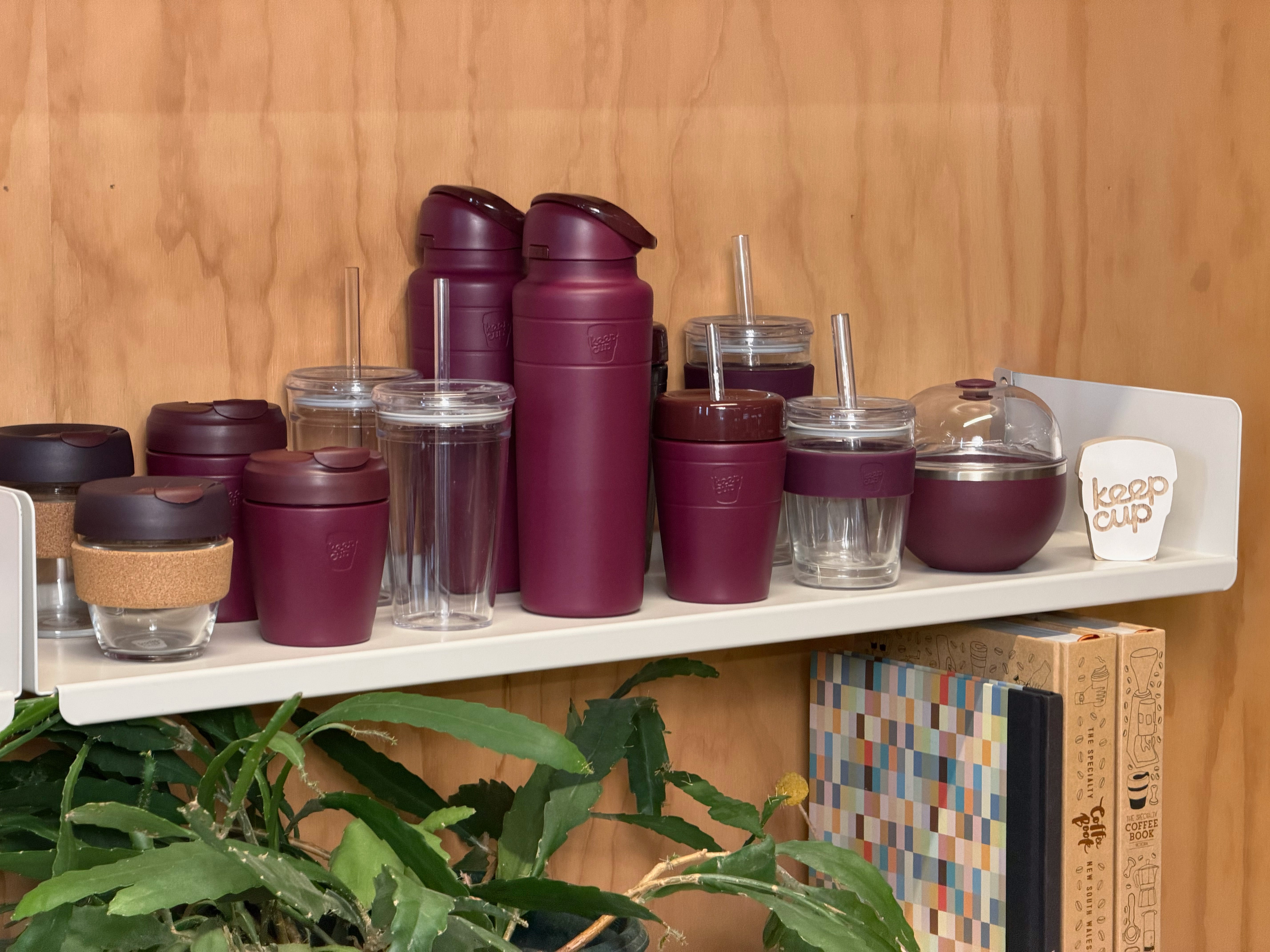 The Mulberry retail range including, Brew Cork, Commuter travel cup, Cold Cup Origjnal, Ora insulated water bottle, Commuter insulated Cold Cup, Cold Cup longplay and Go Bowl Luxe, on a white shelf against a wood-paneled wall.