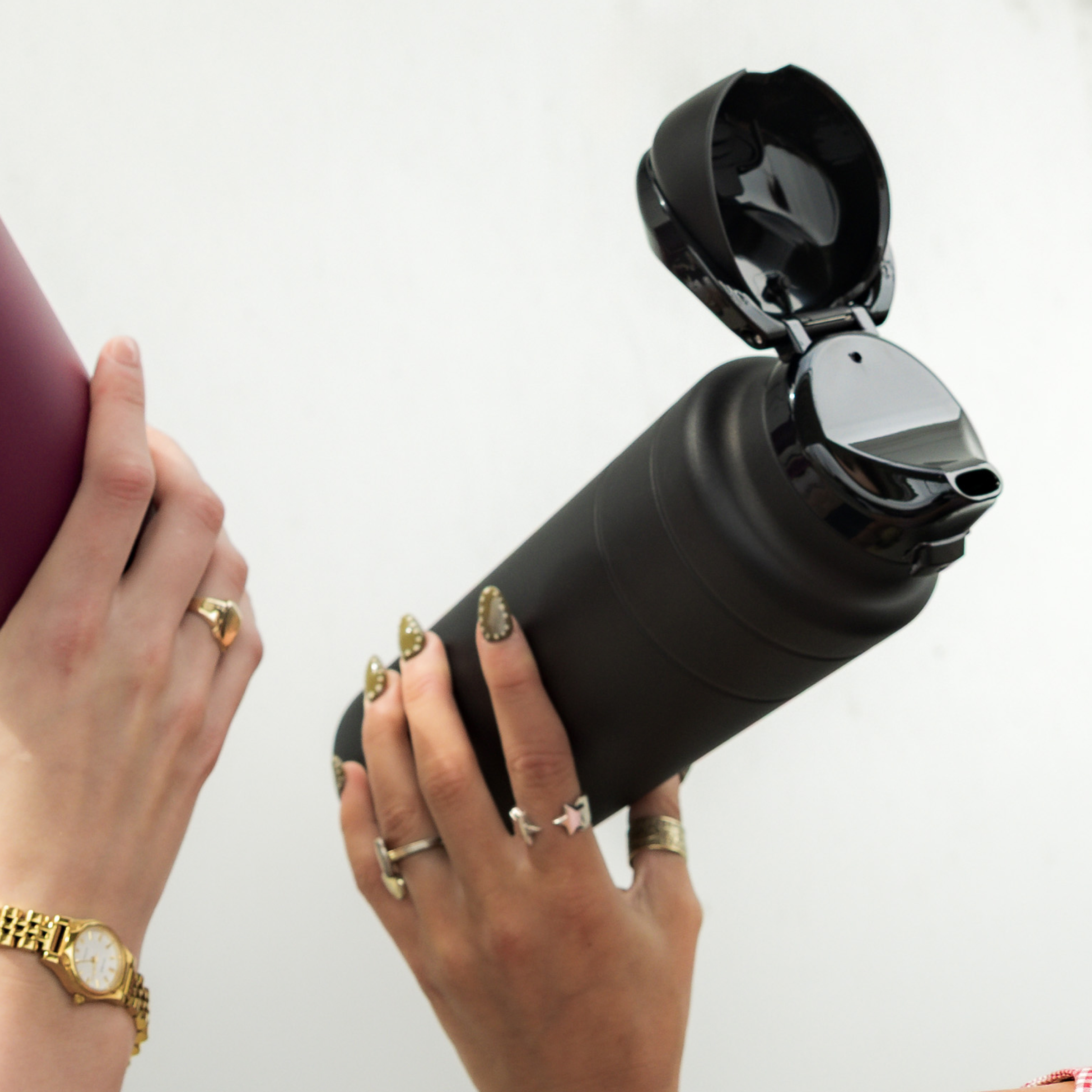Black water bottle with a purple sleeve held by hands with gold rings and a watch.