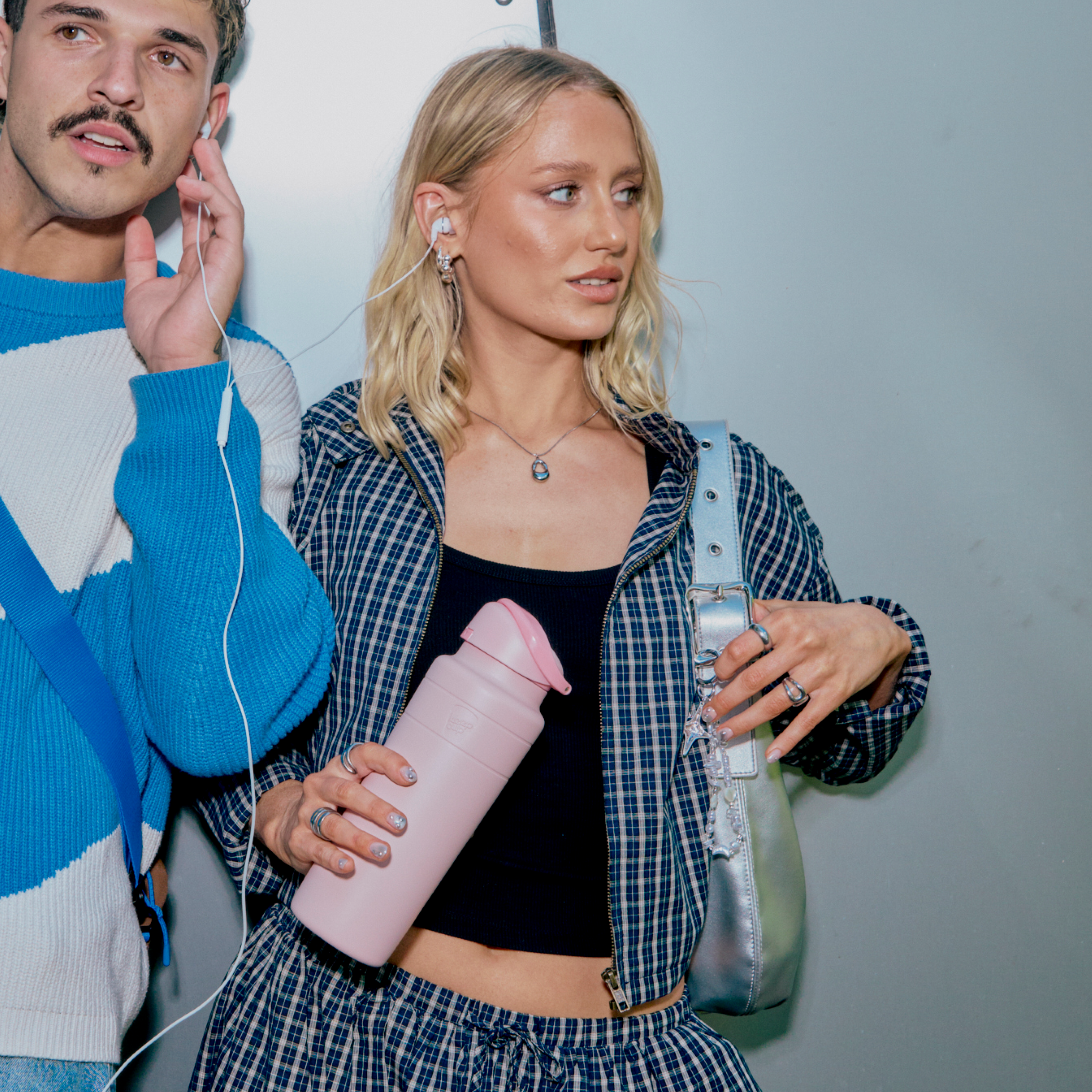 Two people standing next to each other listening to music, one holding a pink water bottle.