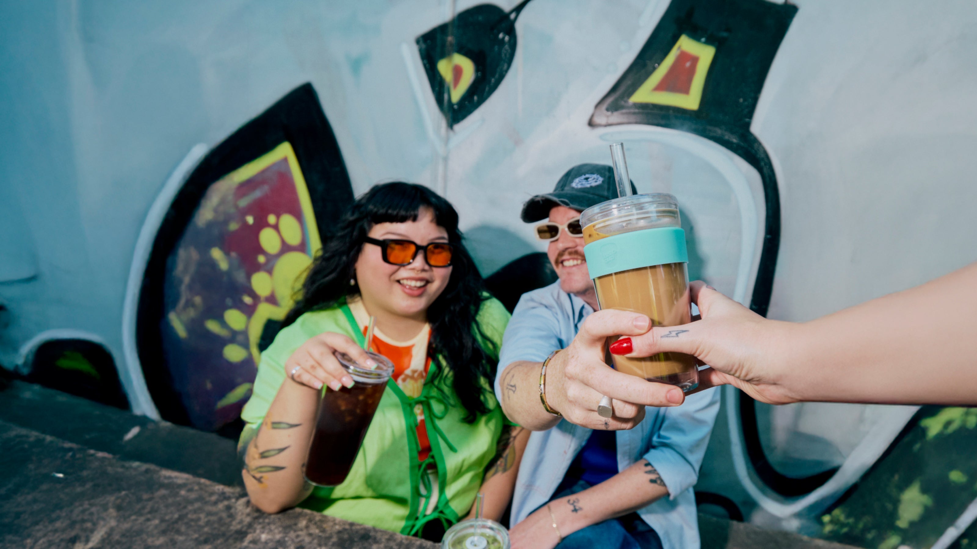 Two people sitting together, one holding a drink, with a colorful background.