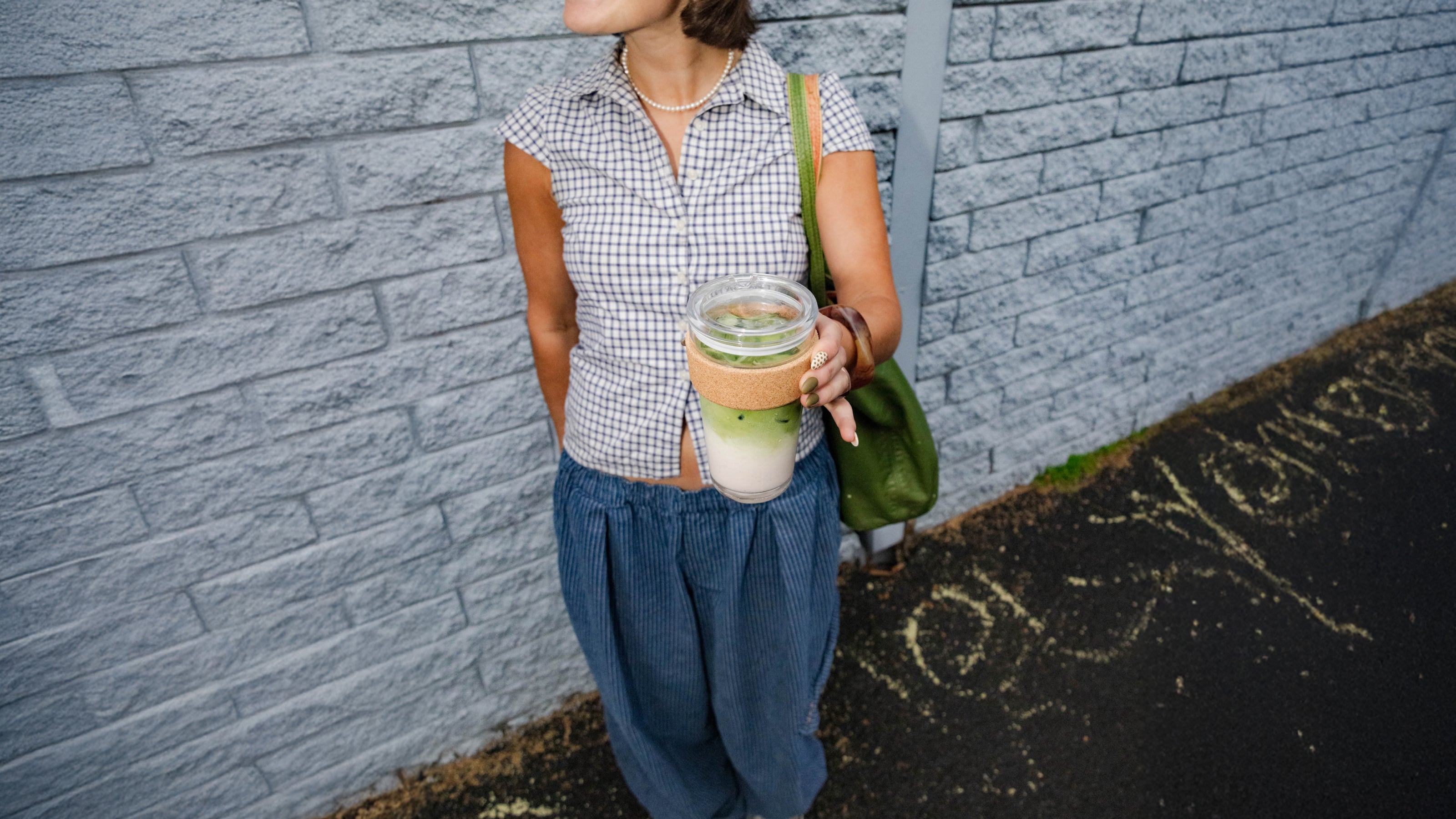 Person holding a drink against a gray brick wall
