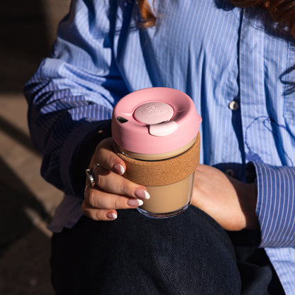 Person holding a pink KeepCup glass reusable coffee cup with cork band