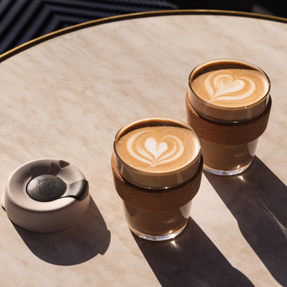 Two KeepCup reusable coffee cups with latte art on a light surface.