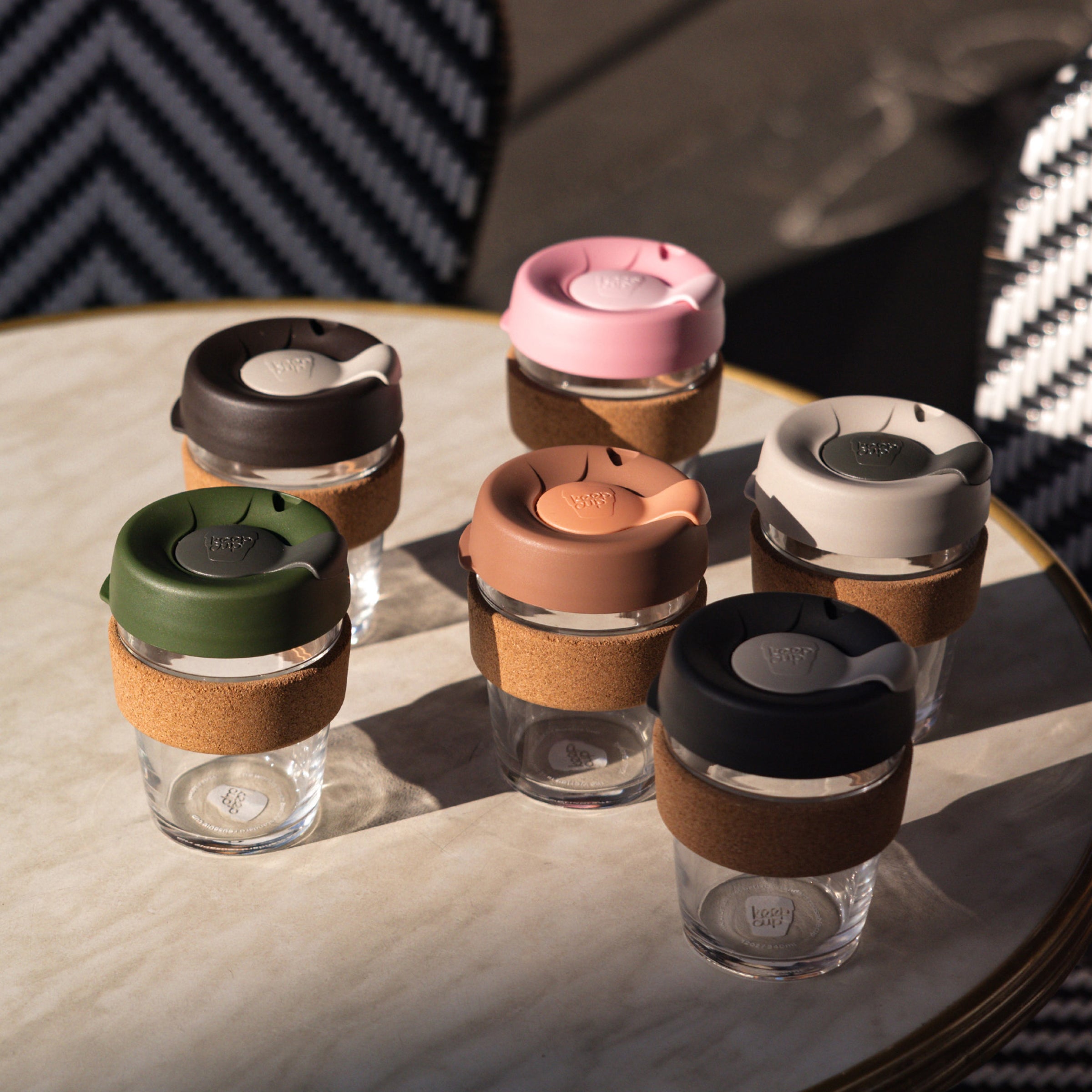 Set of KeepCup glass cups with cork bands in various colourful lids on a marble table