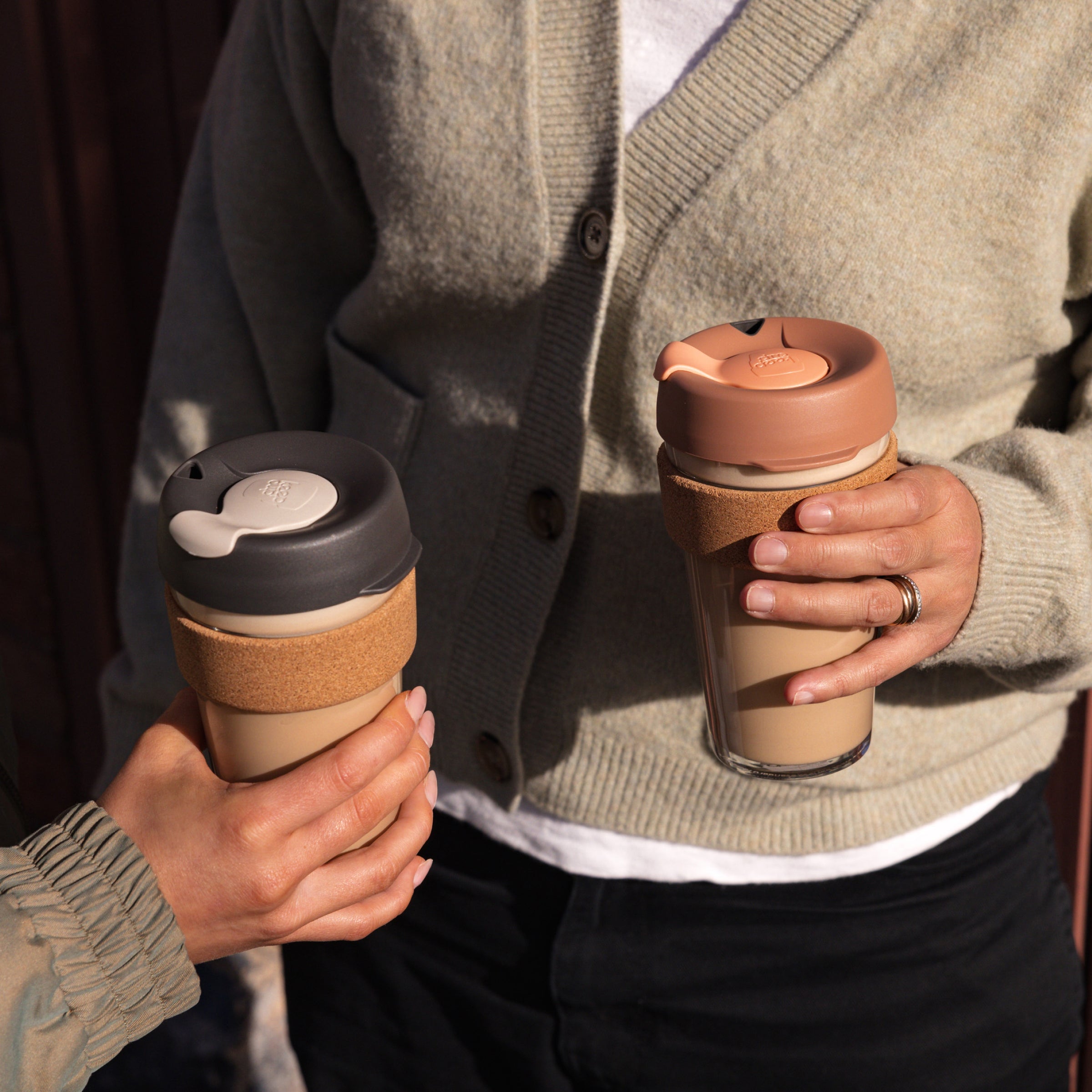 Person holding two KeepCup reusable coffee cups with different lid designs.
