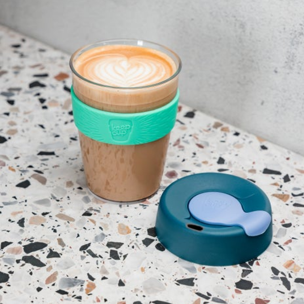 KeepCup reusable coffee cup with a teal silicone band and lid on a terrazzo countertop.