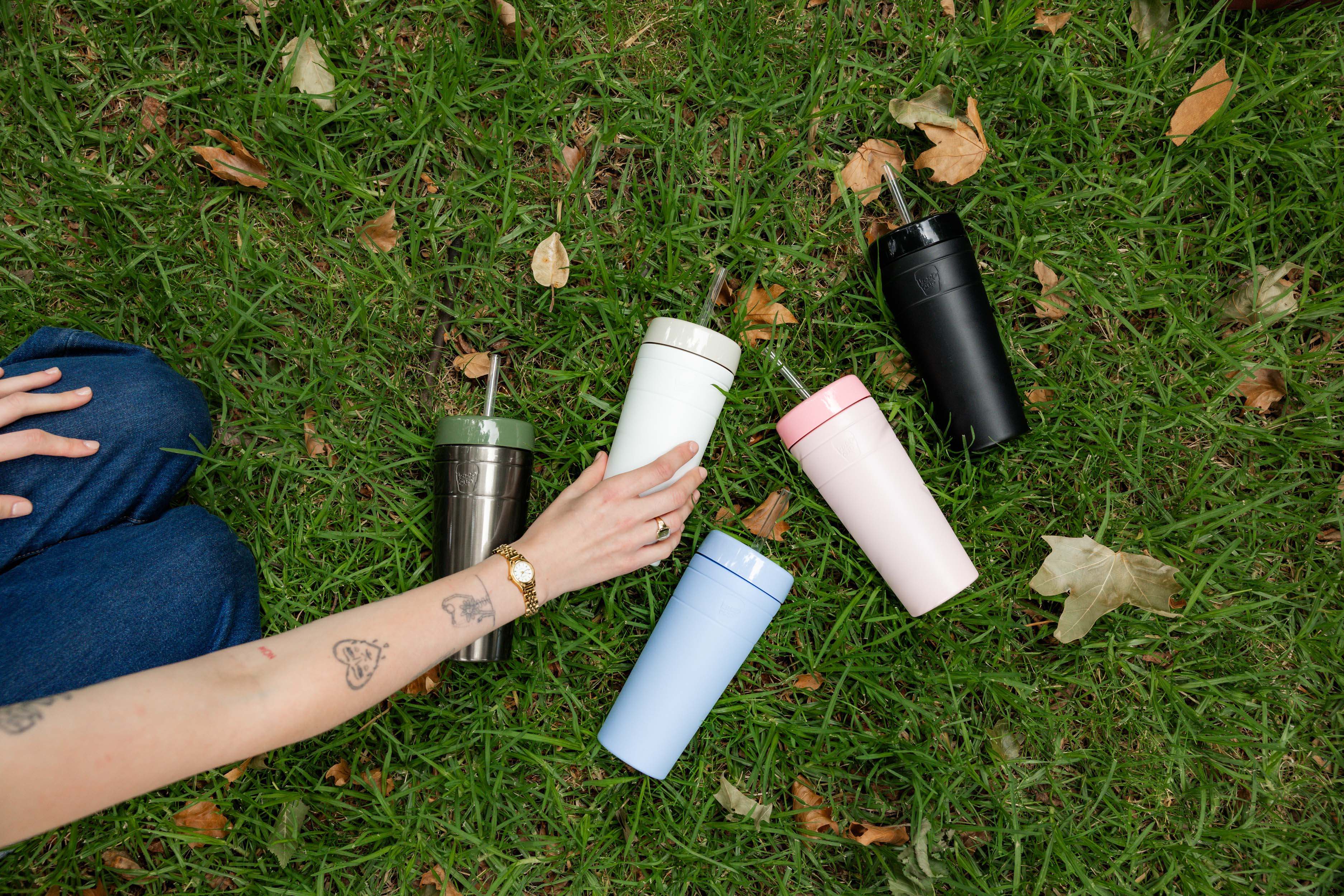 Five colorful tumblers on grass with a hand reaching out