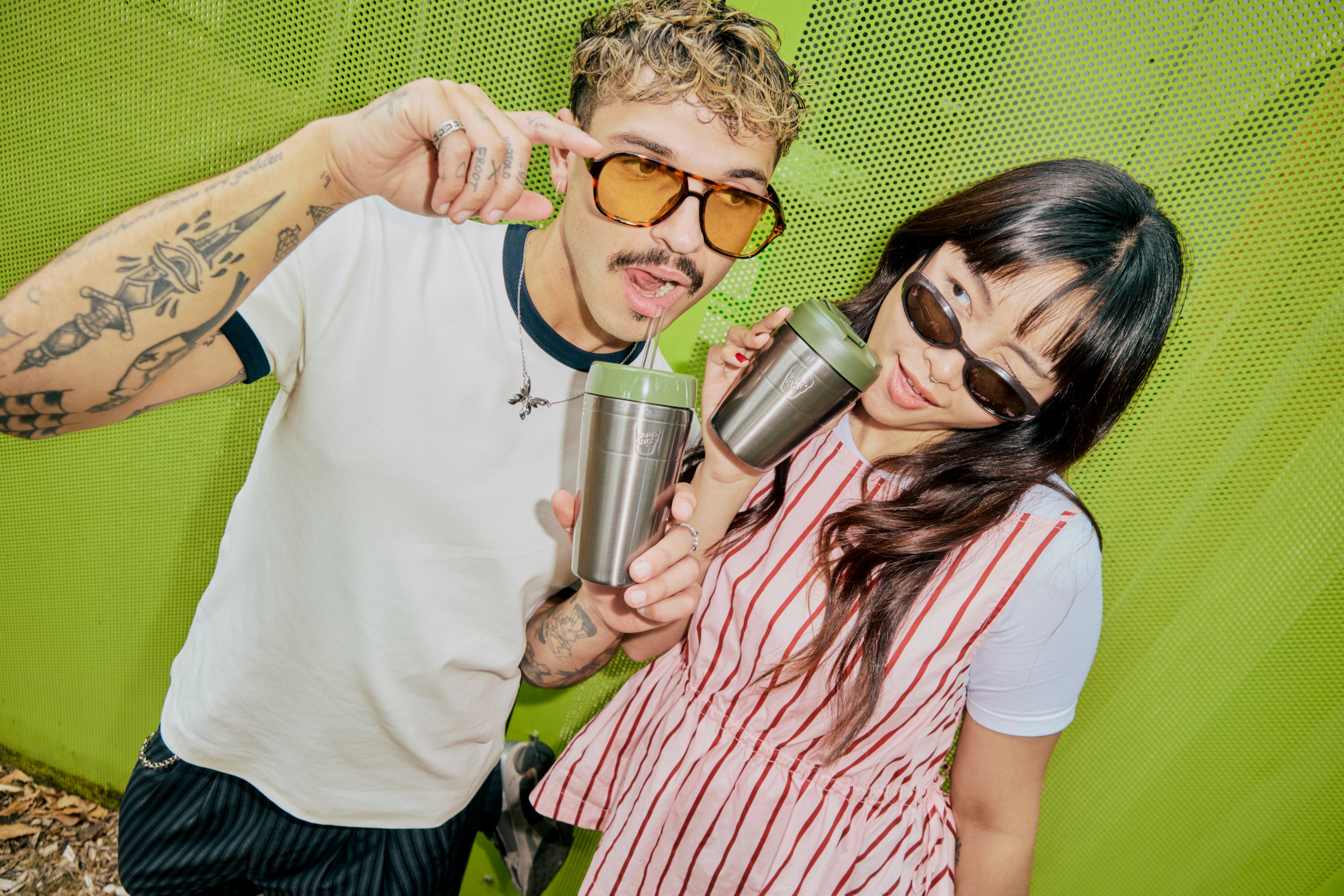 Two people with stainless steel insulated drink bottles featuring lime green lids, photographed against vibrant green backdrop