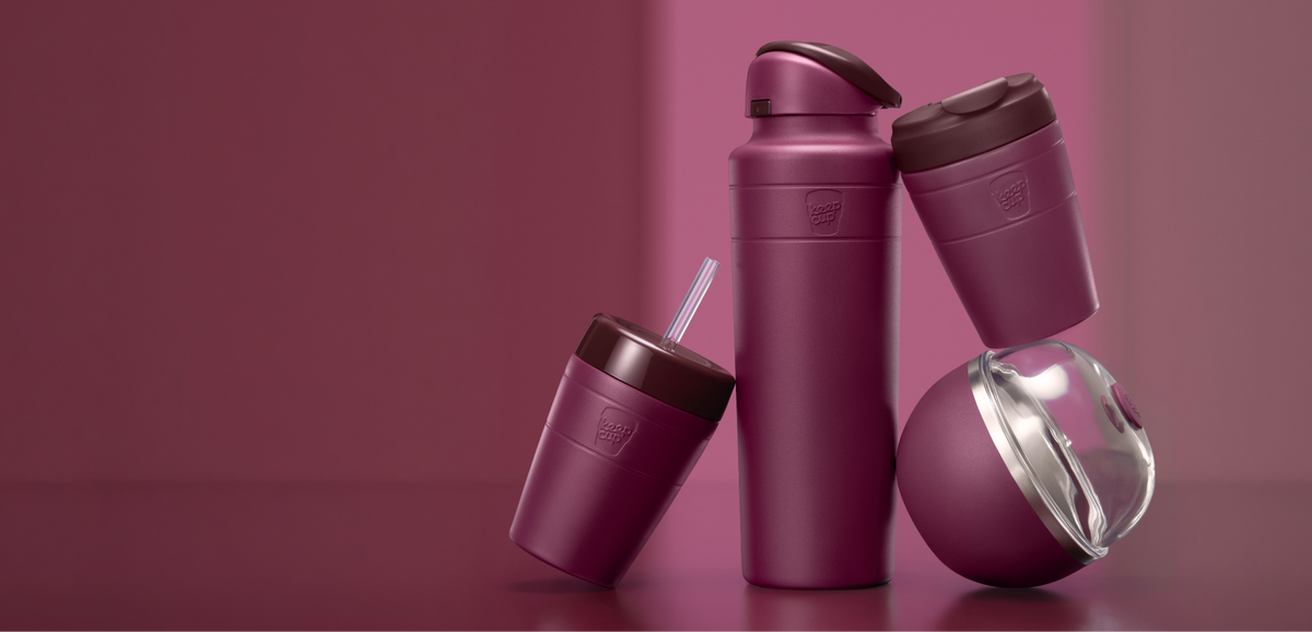 Four reusable travel bottles and tumblers in a Mulberry, arranged on a matching studio surface. The set includes a Commuter Cold Cup, Ora insulated water bottle, Commutera and Go Bowl Luxe