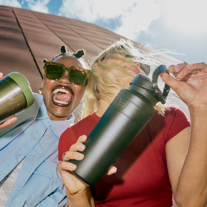Two people holding insulated water bottles outdoors with a clear sky background