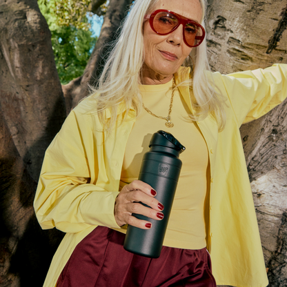 Woman in yellow shirt and sunglasses holding a black water bottle outdoors.
