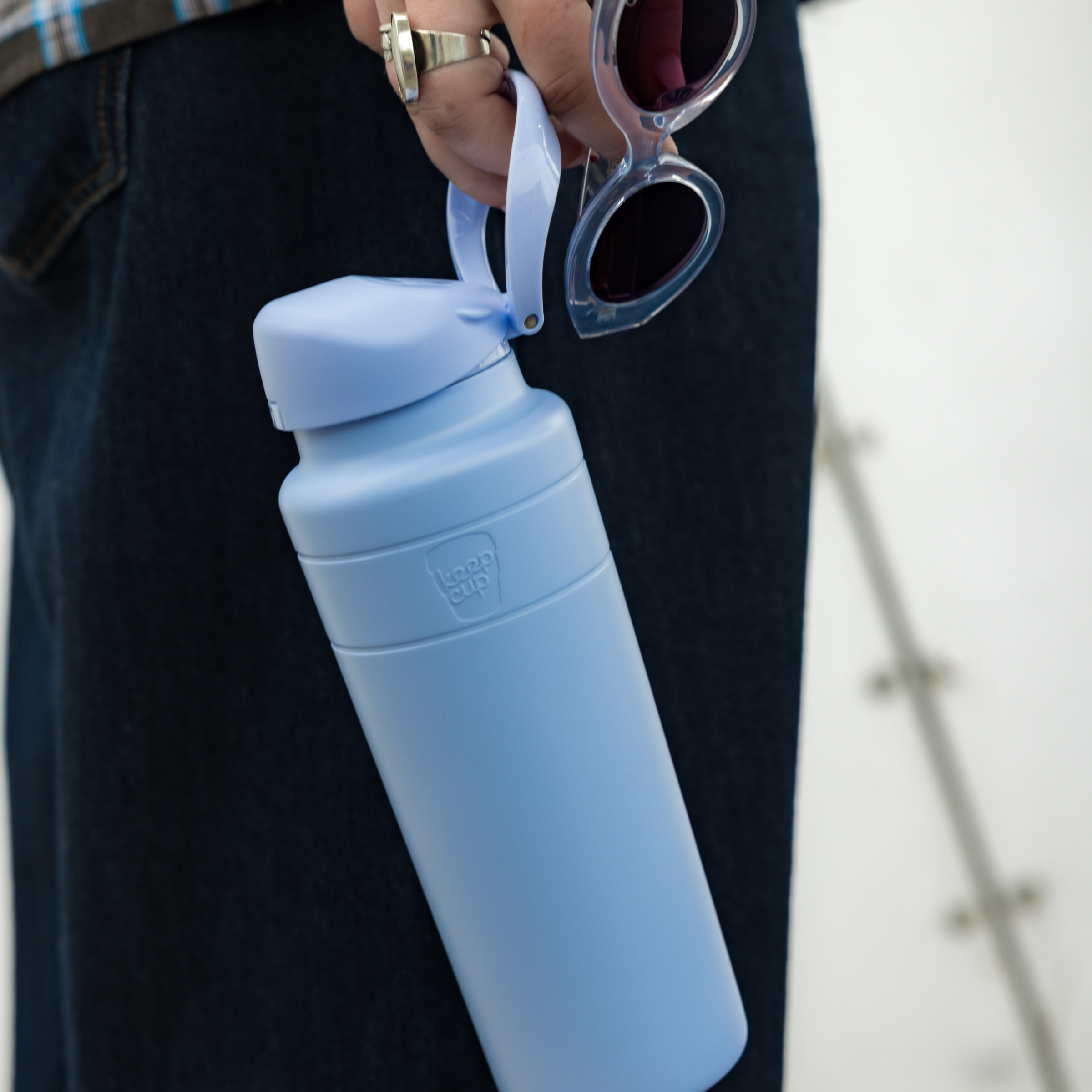 Orchid water bottle with a cap held by a person wearing dark pants.