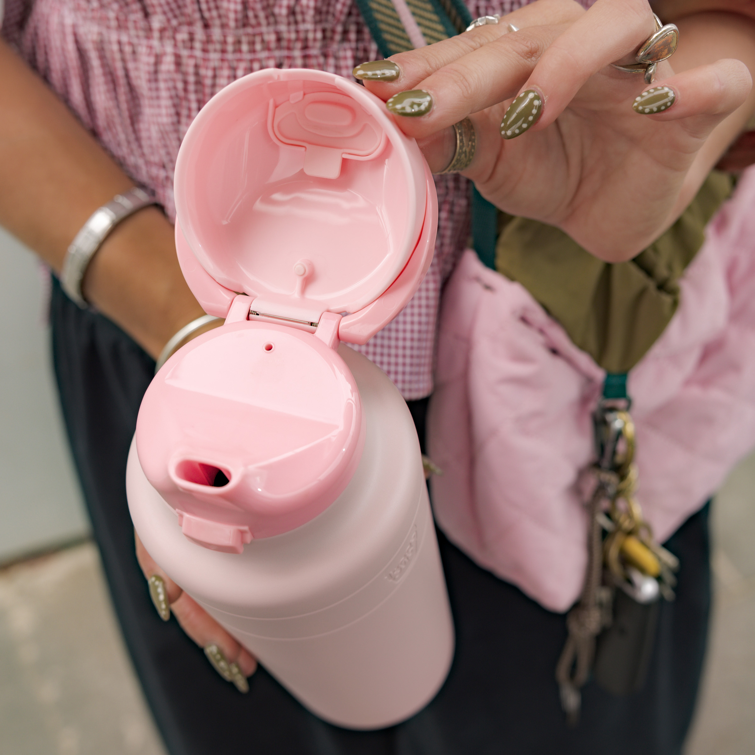 Person holding a pink water bottle with a keychain in the background