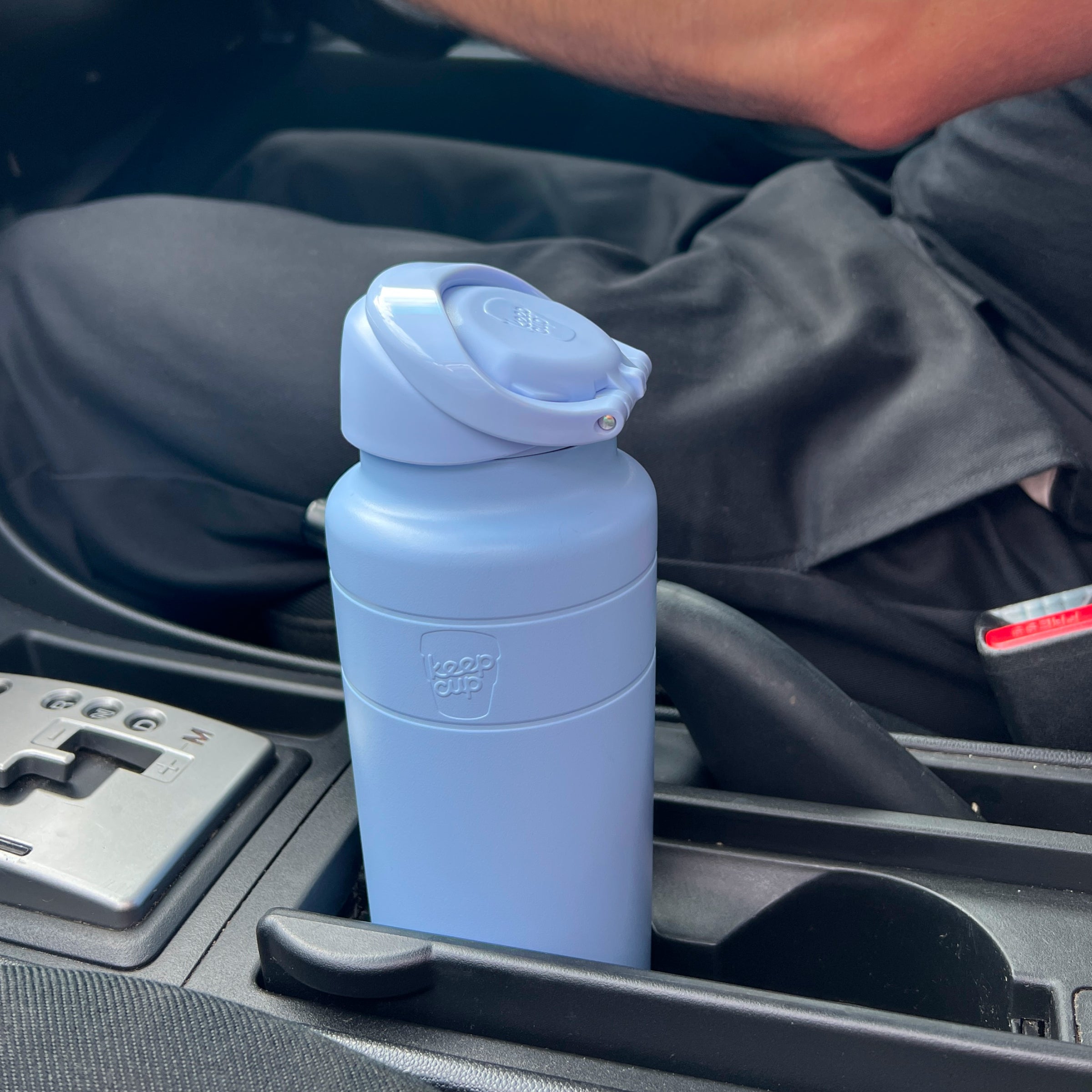 KeepCup Ora Bottle 700ml in Orchid, a matte periwinkle blue insulated bottle with flip-top lid, sitting in a car cup holder next to the gear shift.